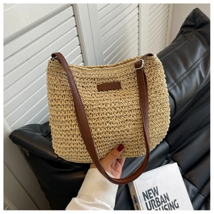 Détail du sac en paille beige avec bandoulière en cuir marron et étiquette décorative