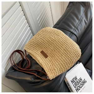 Détail d'un sac bandoulière en paille beige avec sangle en cuir sur canapé noir