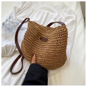 Détail de la texture du sac en paille tissée avec bandoulière en cuir brun sur lin blanc