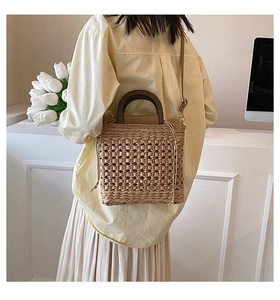 Detail of hand-woven straw tote bag with wood handle and strap in minimalist setting