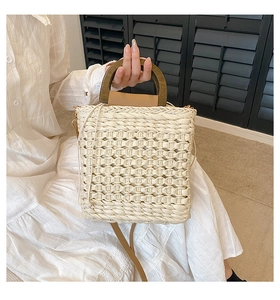 Detail of woven straw handbag with dark brown wooden handle and brown leather shoulder strap