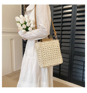Detail of hand-woven straw shoulder bag with brown leather handles and adjustable strap