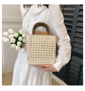 Detail of straw woven handbag with dark brown wooden handles and drawstring closure