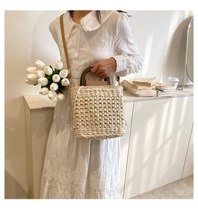 Detail of hand-woven straw bag featuring round wooden handles and adjustable shoulder strap