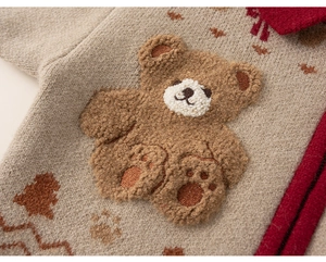 Detail of knit sweater showing red collar trim and 3D brown plush bear patch