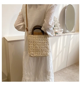 Detail view of woven straw handbag featuring dark wooden handles and leather shoulder strap