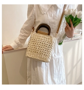 Detail of straw woven tote bag featuring dark wooden handle and beige drawstring closure