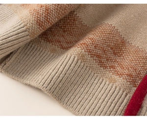 Detail view of the ribbed cuff and orange geometric knit pattern on warm beige sweater