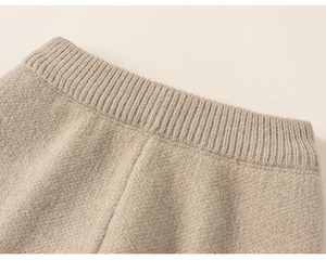 Detailed close-up of wide ribbed elastic waistband on oatmeal knit trousers for girls