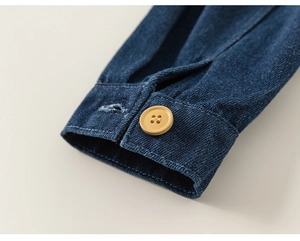 Detail einer dunkelblauen Jeansmanschette mit einem kontrastierenden senfgelben Knopf