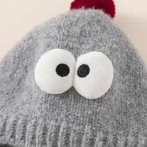 Gray knitted winter hat for kids featuring cute monster eyes and a red pompom on top