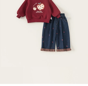 Detail van rode sweater met appelprint en blauwe jeans met hartjesborduurwerk