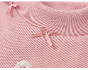 Detail van roze geribbelde thermische set met elastische halslijn en zijden strik met borduursel