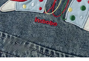 Detail of cartoon patchwork embroidery and brand logo on dark blue denim fabric