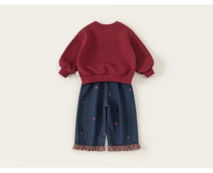 Detailweergave van bordeaux sweatshirt en spijkerbroek met rood borduursel en geruite ruches