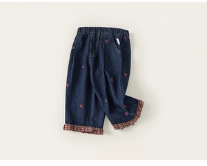 Detail van donkerblauwe kinderjeans met rood borduursel en geruite ruches aan de zoom