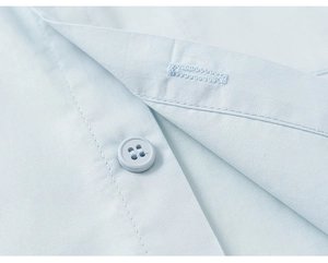Detail of light blue cotton shirt featuring neat stitching and matching round buttons