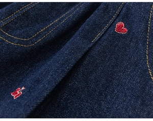 Detail van donkerblauwe denim met rood hart en strikborduurwerk en gele stiksels