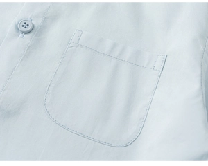 Close-up of light blue shirt pocket detail with fine stitching and resin button