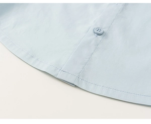 Close-up of light blue shirt hem and button placket detail with clean stitching