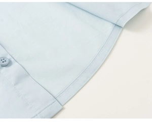 Detailed close-up of light blue shirt hem with clean double stitching and button