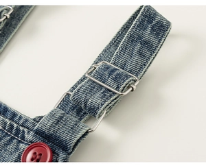 Macro detail of blue denim shoulder strap with silver metal buckle and red button