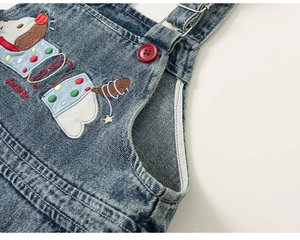 Detail view of cartoon dog embroidery and red button on navy denim overalls for kids