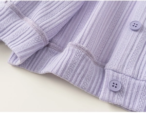Detail of purple ribbed knit fabric with matching round buttons and woven hemline