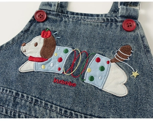 Close-up of kids denim overalls featuring a colorful cartoon dog patch and red buttons