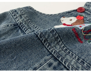 Detail of denim fabric with cartoon puppy embroidery and insbobo lettering on girls top