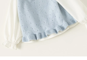 Detail of light blue knit vest with hollow patterns and white ruffle sleeve shirt