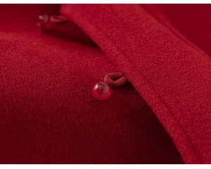 Détail du tissu en laine rouge et du bouton traditionnel en perles sur un gilet pour enfant