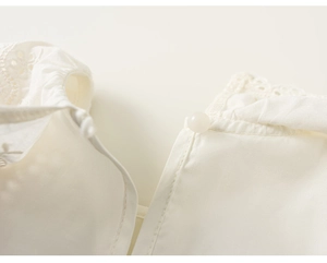 Detailed view of white cotton lace collar with hollow embroidery and pearl button closure