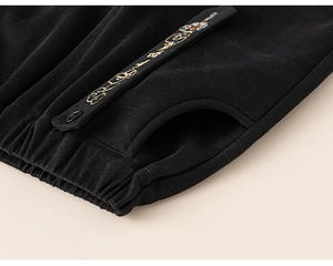 Detailed macro view of black kids' trousers showing elastic waistband and gold embroidery