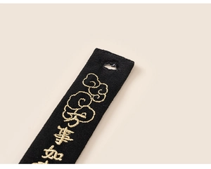 Close-up of black fabric pendant with gold embroidered cloud patterns and Chinese characters