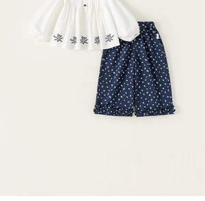 Detail of white cotton top with blue floral embroidery and matching ruffled hem pants