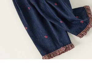 Détail du jean fille avec broderie coeur rouge et ourlet à carreaux à volants