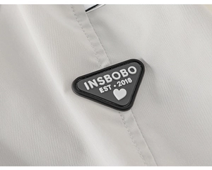 Detailed macro view of a triangular rubber badge with INSBOBO logo on grey cargo pants