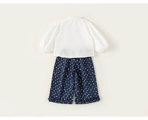 Detail of girls' white cotton blouse with ruffled collar and floral printed trousers