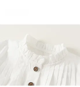 Detail view of girl's white shirt collar featuring textured pleats and dark buttons