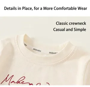Detail of baby girl's cream knitted t-shirt featuring a ribbed crew neck and letter print