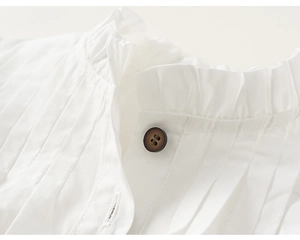 Detail of white cotton shirt neckline featuring ruffle edges and dark button closure