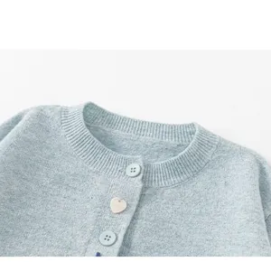 Detailopname van de ronde hals van een lichtblauw gebreid vest met hartvormige knoop