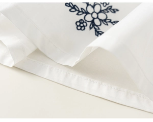 Detail of white fabric featuring delicate navy blue floral embroidery and neat hem stitching