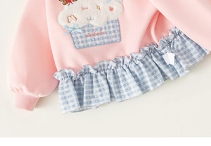 Detail van roze meisjessweater met cupcake-borduurwerk en gingham ruches aan de zoom
