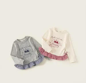 Detail of kids long sleeve T-shirt with cake print and plaid ruffle hem on cream fabric