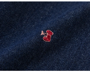 Vue détaillée de la broderie cerise en forme de cœur rouge sur tissu denim bleu foncé