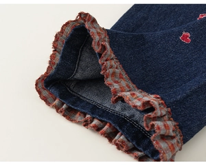Détail du pantalon en jean pour filles avec broderie de cœur rouge et bordure en dentelle