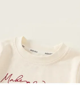 Detail of ribbed neckline on cream cotton kids shirt with red script embroidery