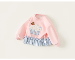 Detail van roze meisjessweater met geborduurde cupcake beer en blauwe ruitjesrand